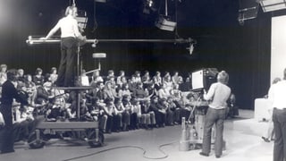 Ums da camera che filmeschan il public d'ina emissiun da televisiun. Ums da camera che filmeschan il public d'ina emissiun da televisiun.