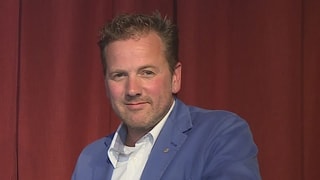 Purtret da Christian Jott Jenny cun tschop blau davant ina tenda cotschna.