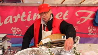 In um cun ina chapetscha cotschna davos in stan da fiera. avant el in priel cun en peschs.