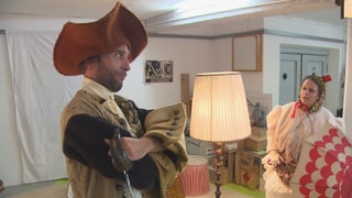 Dus acturs en costums. Stgilat cun in grond chapè da pirat. Giaglina cun parisol.