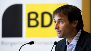 Purtret da Gian Michael, cun davostier il logo mellen e nair da la PBD.. 
