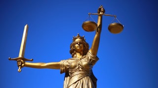 Purtret da la justicia che porta in bindel sur ils egls, ina spada en in maun ed ina stadera en l'auter. 