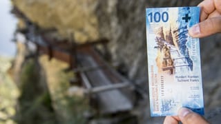 Dus mauns che tegnan ina bancnota da 100 francs.