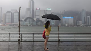 Ina dunna cun in parisol nair stat davant ina saiv - davostiers vesan ins la citad da Hongkong ch'è tut turbla pervi dal taifun.