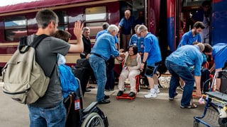 Voluntars che gidan a persunas en sutgas da rodas en il tren. 
