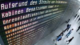 Passagiers da la Lufthansa stattan davant ina tavla che declara ch'ils sgols èn stritgads pervi da la chauma dal persunal da cabina