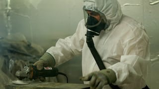 In um en vestgì da protecziun alv e cun mascra da fladar dismetta asbest