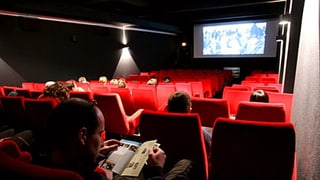 Sala da kino cun intginas persunas che sesan