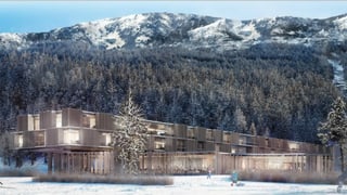 Fabricat lung cun fatschada da lain, fanestras per part illuminadas, davos la muntogna.