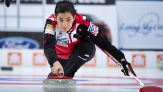 Giugadra da curling en schanuglias stumpla cun in maun il crap e cun l’auter tegna ella la scua.