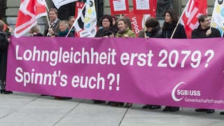 Ina gruppa da persunas tegn in placat lung viloet cun scret si "Lohngleichheit erst 2079? Spinnt's euch?!"