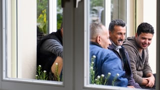 trais requirents d'asil sesan avant la chasa, vista tras la fanestra