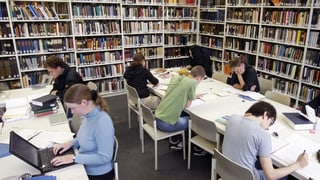 Studentas e students lavuran en ina biblioteca.