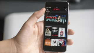 Purtret d'in maun che tegna in telefonin ed ha avert l'app da netflix. Purtret d'in maun che tegna in telefonin ed ha avert l'app da netflix.