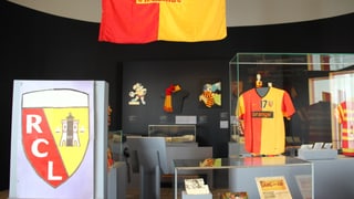 Differents objets da fans en vitrinas. In t-Shirt, ina schlingia, Bandieras, bindels. La vopna dal club è cotschen e melen cun scret RCL lien