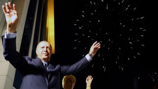 Purtret dad Erdogan che tegna ils mauns en l'aria.