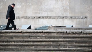 Purtret d'in um che passa dasper ina tavla da commemoraziun ora. Davostier sin la paraid stat scrit: «Den Opfern der nationalsozialistischen Gewaltherrschaft».