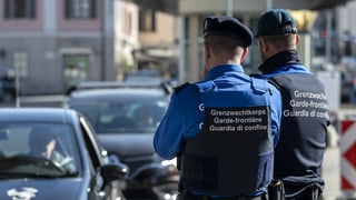 Dus emploiads da la guardia da cunfin observan ils autos che passan la duana.