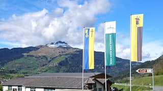 L'entrada al club da golf cun las bandieras dal club, da Schluein e Sagogn. Davostiers il Piz Mundaun.