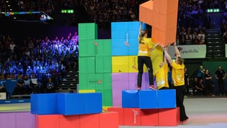 Trais atlets en T-Shirts mellens emplunan elements da Tetris - davostiers vesan ins il public sin tribuna.