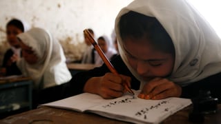 mattatscha che scriva en ses carnet en ina scola en l'Afganistan