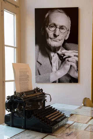 Ins vesa ina fotografia da Hermann Hesse pendì si en il museum Hermann Hesse a Montagnola e davant sin maisa ina maschina da scriver dal scriptur.