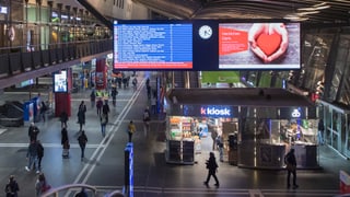 Staziun da tren cun in kiosc e passagiers sin ils perruns.