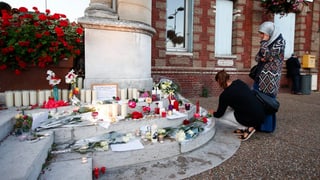 Duas dunnas mettan chandailas e flurs sin la stgala da la baselgia nua ch'i aveva dà in attentat mardi