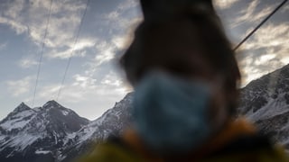 purtret d'ina persuna che porta ina mascrina davant ina culissa da muntogna. 