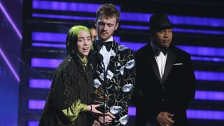 Purtret da Billie Eilish e ses frar Finneas sin tribuna, Billie tegna il premi e discurra en il microfon fertant che ses frar stat dasper ella. Purtret da Billie Eilish e ses frar Finneas sin tribuna, Billie tegna il premi e discurra en il microfon fertant che ses frar stat dasper ella.