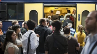 Glieud che spetga davant la porta averta d'in tren.