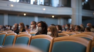 Persunas cun mascrina da protecziun en ina sala da concert. Be paucs sezs èn occupads.