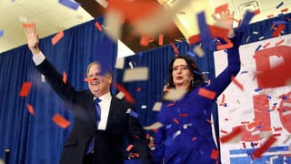 Purtret da Doug Jones e sia dunna che dattan maun, davanttiers croda confetti alv, cotschen e blau giu dal plaun sura. 