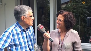 Eugen Caduff avant il microfon d'Alice Bertogg. E. Caduff porta ina chamischa cun caro blau. El ha chavels grischads.