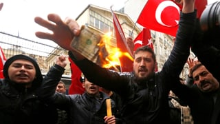demonstrants davant l’ambassada dals Pajais Bass ardan ina nota da dollar.