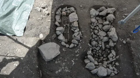 Archäologische Ausgrabung mit Skelett und Steinen im Boden.