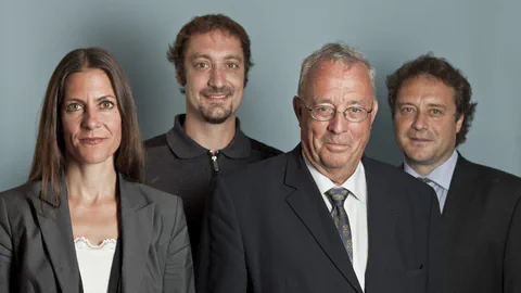 Vier Personen in formeller Kleidung vor blauem Hintergrund.