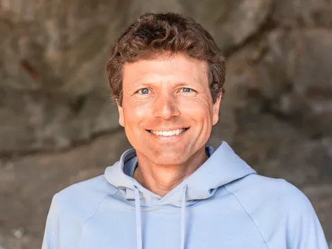 Mann mit blauem Hoodie lächelnd vor Felswand.