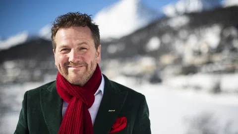 Mann in rotem Schal vor verschneiten Bergen.