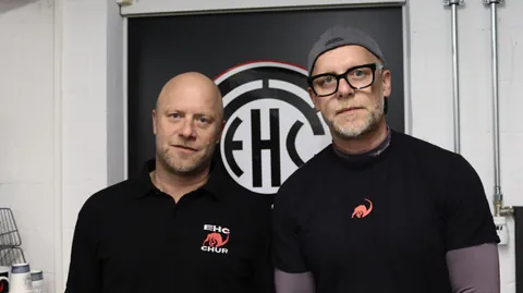 Zwei Männer stehen vor einem EHC Chur Logo.