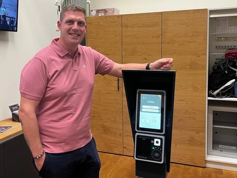 Person in rosa Hemd steht neben einem elektronischen Gerät.