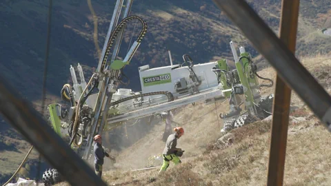 Arbeiter bedienen grosse Maschine auf steilem Hügel.