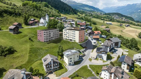 Luftaufnahme eines Dorfes in hügeliger Landschaft mit Kirche und Wohngebäuden.
