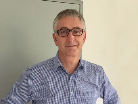 Mann mit Brille und kariertem Hemd steht vor grauer Tür.