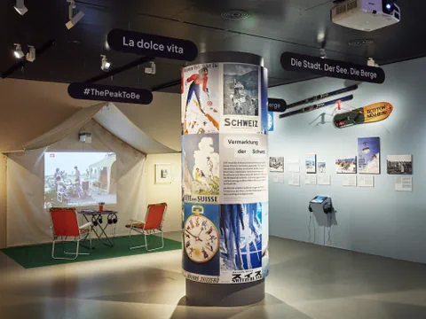 Ausstellungsraum mit Plakaten und Fotos an den Wänden, Tisch und Stühlen.