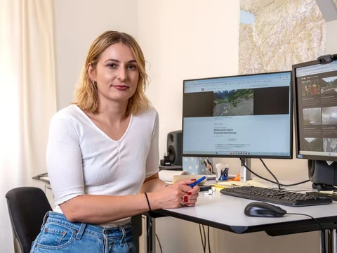 Frau sitzt am Schreibtisch mit zwei Monitoren.