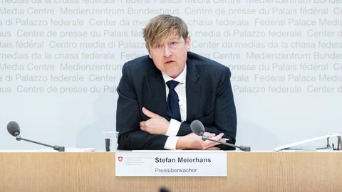 Person spricht bei einer Pressekonferenz am Tisch mit Mikrofonen.