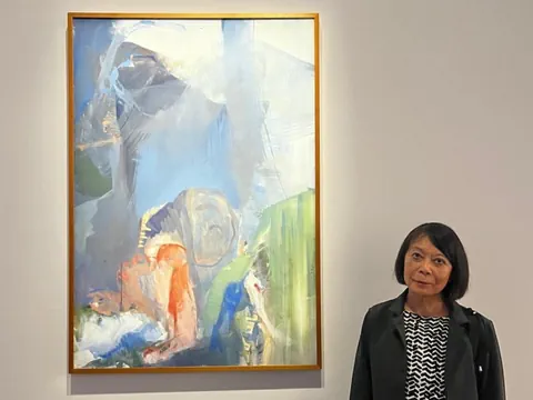 Frau steht neben abstraktem Gemälde in Galerie.