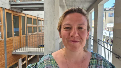 Frau lächelnd auf einem Balkon mit modernem Gebäudedesign im Hintergrund.
