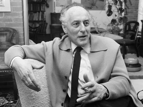 Schwarzweissfoto eines Mannes in einem Wohnzimmer sitzend, im Gespräch.